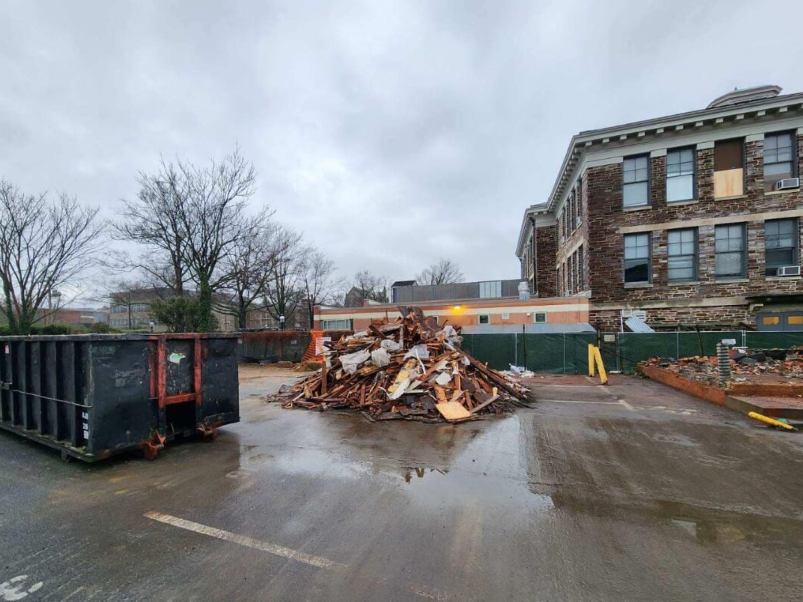Construction site featuring a pile of debris, dumpsters, and an old building under renovation on a cloudy day.