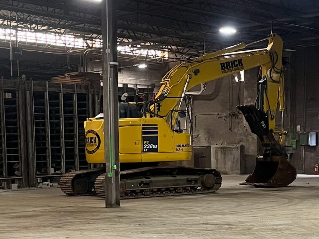 Komatsu excavator branded with 'BRICK' logo inside an industrial plant, showing equipment used in dismantling operations.