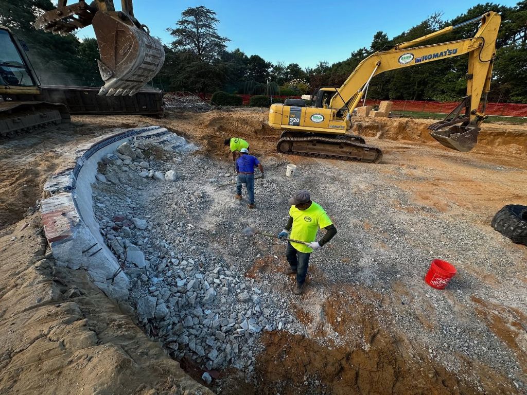 Komatsu excavator with workers clearing rubble at an industrial plant site.