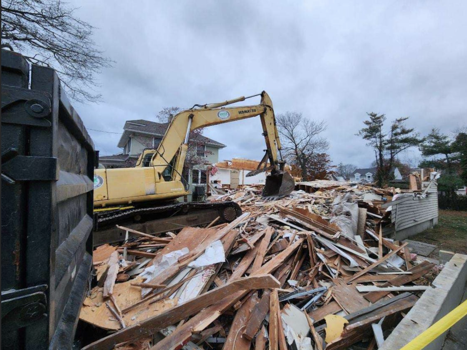 A bulldozer clears debris from a demolished house, showcasing the ongoing construction site.