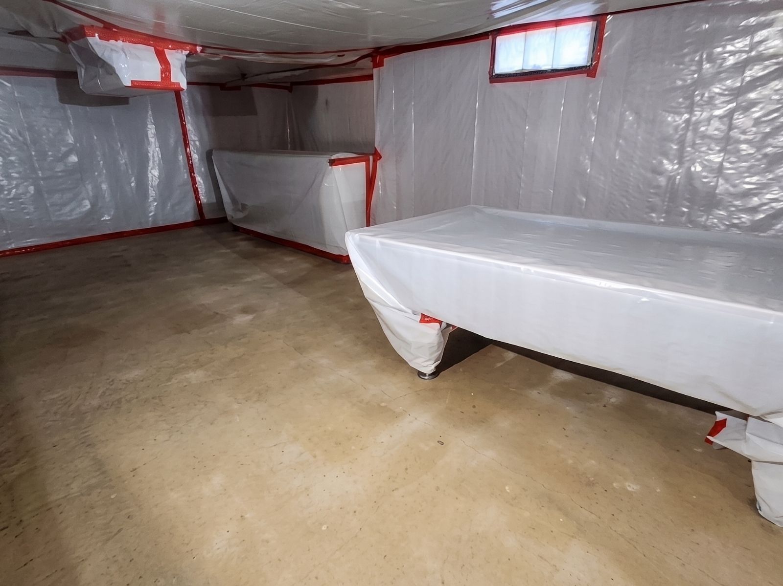 Asbestos abatement containment area in an Ocean County basement with plastic sheeting barriers, sealed openings, and protected furnishings prepared for safe asbestos removal.