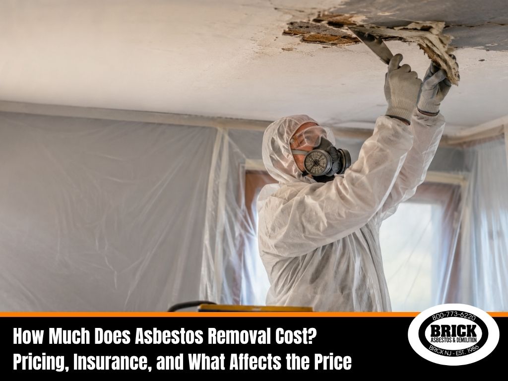 Worker in hazmat suit removing damaged ceiling material, illustrating asbestos removal costs.