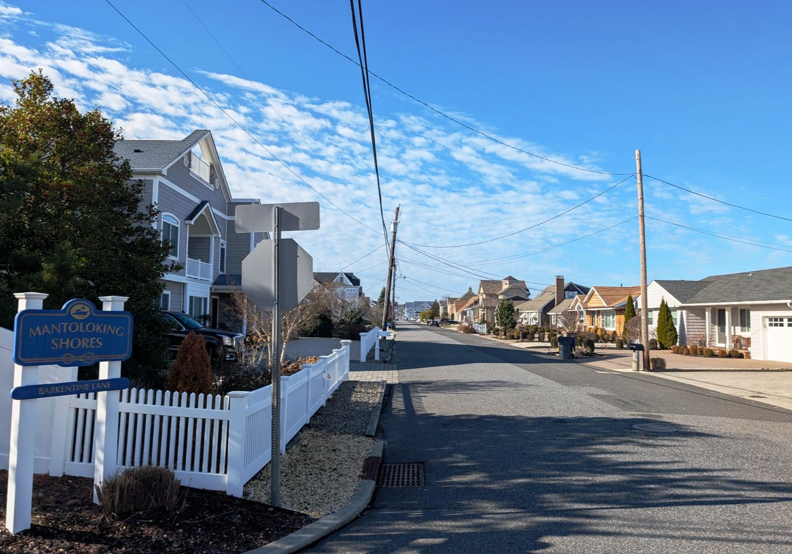 Mantoloking Shores residential street with houses on both sides, blue skies, and a street sign visible.