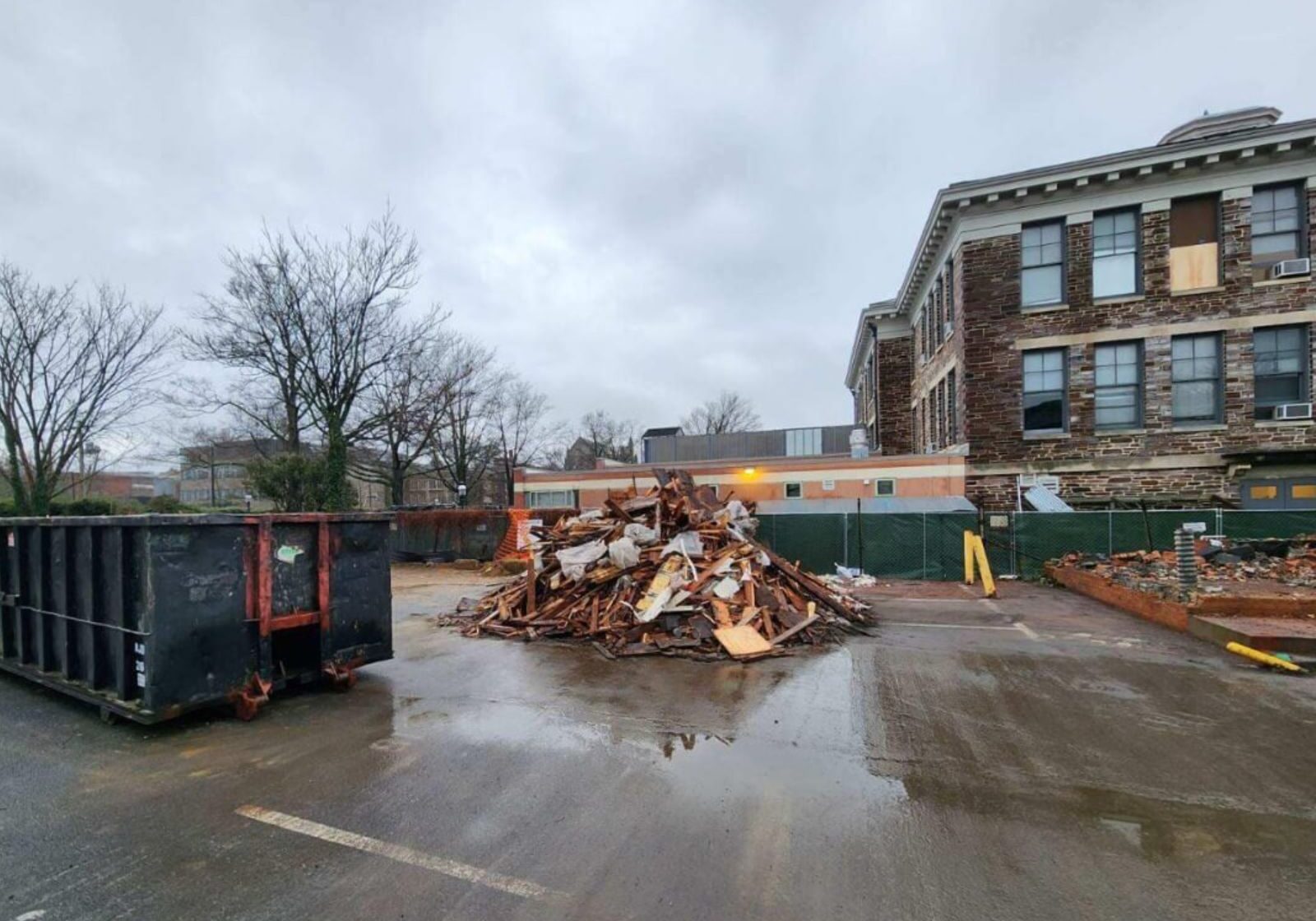 Construction site featuring a pile of debris, dumpsters, and an old building under renovation on a cloudy day.